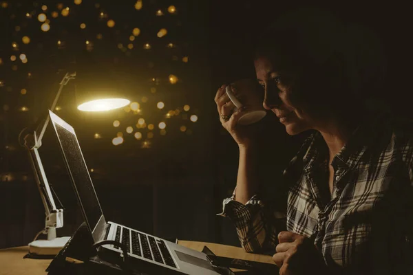 A woman sits at home at night and works on the computer.