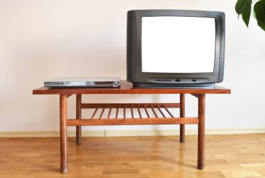 Bir DVD oynatıcı ve modası geçmiş beyaz ekranlı siyah bir TV 1990 'ların apartmanında eski bir masada oturuyor..