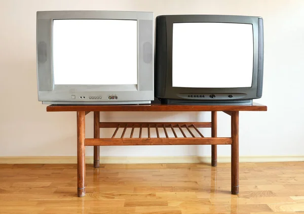Two outdated vintage TVs with blank white screens sit on a vintage table in a 1990s apartment block.