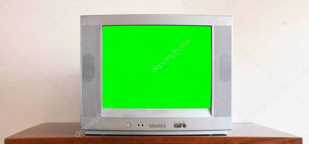 An outdated vintage silver TV with a blank green screen sits on a vintage table in a 1990s tenement house.