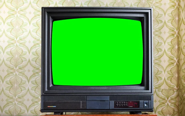 Antique TV with green screen on an antique wooden cabinet, old design in a house in the style of the 1980s and 1990s.