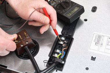 Profesyonel bir elektrikçi, yemek pişirme indüksiyon yüzeyindeki bağlantı kalitesini, bağlantıyı ve voltajı bir testçinin yardımıyla kontrol eder. Elektrikli ocakta sorun var..