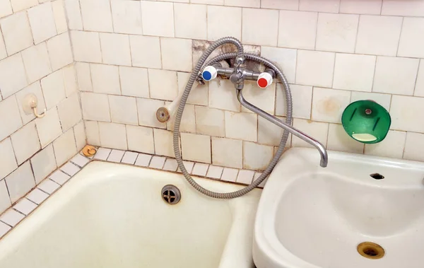 Dirt and mold in the old bathroom on the grout and tiles near the taps. Old plastic tiles on the walls.