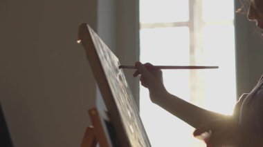 Silüet içindeki bir sanatçı, sıcak güneş ışığıyla aydınlanan, sanatsal ruhu canlandıran huzurlu, güneşli bir ortamda yaratıcılığı ve ilhamı somutlaştıran bir resim yapar.