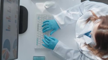 Laboratuvar önlüğü ve eldivenleriyle odaklanmış bir araştırmacı bir klavyeye yazarak monitörde gösterilen verileri analiz ediyor. Sahne, bilimsel araştırma ve veri analizinin özünü yakalıyor..