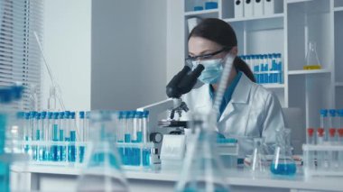 Laboratuvar önlüğü giymiş kendini adamış bir bilim adamı güçlü bir mikroskop altında ileri düzey bir laboratuvardaki araştırmaların önemini vurgulayarak gelecekteki yenilik ve keşifleri örnek alarak test örnekleri üzerinde çalışıyor.