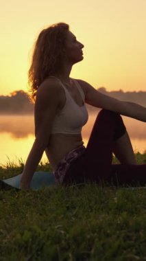 Bir kadın şafak vakti sakin göl kıyısında yogaya girişir, gündoğumunun güzel altın renklerini kucaklayarak farkındalığı, sağlığını ve çevresindeki doğayla derin bir ahengi sağlar.