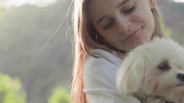 Yumuşak ve iç açıcı bir etkileşim genç bir kadının tüylü köpeğini sevgi dolu bir şekilde sakin ve sakin bir arka planda kucaklaması, sıcaklık, neşe ve güçlü bir arkadaşlık hissi yayması gibi.