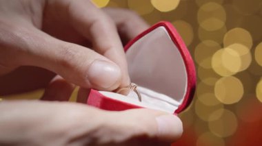 Lüks bir kırmızı kutudan ortaya çıkan hassas bir yüzüğün yakın çekimi samimi bir teklifi yakalar. Rüya gibi arka plan, aşk ve bağlılığın göstergesi olarak romantik atmosferi güçlendirir.