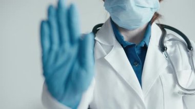 Beyaz önlüklü ve eldivenli bir sağlık çalışanı, cerrahi maske takarken dikkat göstererek, sağlık ortamlarındaki herkesin sağlığını korumak için güvenlik protokollerinin önemini vurgular.