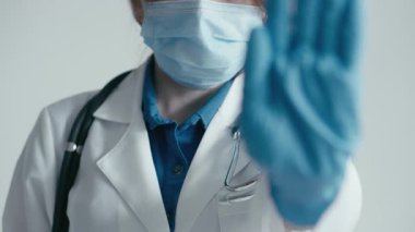 Yoğun bir tıbbi ortamda, beyaz önlüklü ve maskeli bir sağlık uzmanı eldivenli bir el uzatarak, güvenlik, hijyen ve hasta bakımına olan bağlılığını günümüzde sağlık ortamında vurguluyor.