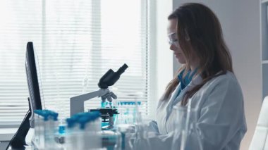 Kendini adamış bir bilim adamı mikroskop altında, modern araştırmaları örnek alan ve canlı bir laboratuvar ortamında yaratıcılığı teşvik eden gelişmiş laboratuvar ekipmanlarıyla çevrelenmiş biyolojik örnekleri gözlemler.