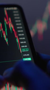 Yakın plan bir resim, önemli borsa verilerini gösteren akıllı bir telefonu kavramayı, canlı ticaret dinamiklerini ve dijital platformlardaki pazar analizlerine kolay erişimi vurguluyor