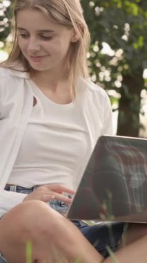 Genç bir kadın, canlı bir bahçede yumuşak bir battaniyeye uzanıyor. Küçük köpeği yakınlarda oynarken bilgisayarını neşeyle kullanıyor. Mükemmel bir rahatlama ve doğal güzellikle bağ kuruyor.