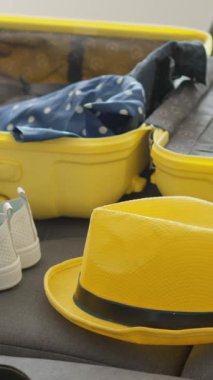 Parlak sarı bir bavul, içi seyahat gereksinimleriyle dolu iyi korunmuş bir iç mekan gösteriyor. Yakınlarda, taze beyaz ayakkabılar, parlak sarı bir şapka ve önümüzde heyecan verici maceraları bekleyen bir kamera.