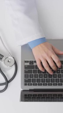 Steteskop ve hasta belgeleriyle çevrili bir dizüstü bilgisayardaki tıbbi profesyonel tipler, verimli dijital kayıt tutma odaklı modern bir sağlık ortamını vurguluyor.