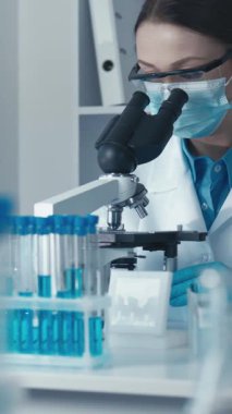 Beyaz laboratuvar önlüklü kendini adamış bir bilim adamı ileri laboratuvar ekipmanlarıyla çevrili örnekleri mikroskop altında inceliyor ve araştırmada hassasiyet ve doğruluğun önemini vurguluyor.