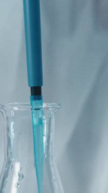 Bir laboratuvarda, yetenekli bir bilim adamı canlı bir mavi sıvıyı yönetmek için bir pipet kullanır, bilimsel araştırmalarda hassasiyet ve doğruluk ve yenilik gerekliliğini vurgulayarak çeşitli alanlarda ilerlemeyi sağlar.