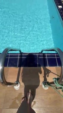 Gölge silueti havuz merdiveninden turkuaz suya iniyor, POV perspektifi ayaklar ve yansıma, parıldayan dalgalar