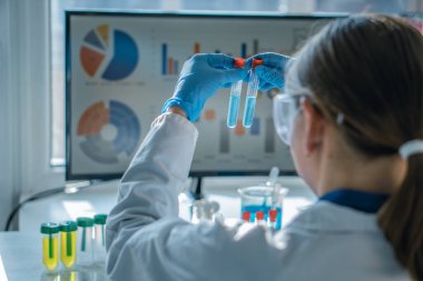 Kadın araştırmacı, yüksek teknoloji laboratuvar ortamında test tüpleri kullanarak kimyasal analiz yapıyor. Veri görselleştirme ve laboratuvar ekipmanları bilimsel ilerleme ve keşfi vurguluyor