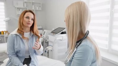 Bir kadın, çağdaş bir klinikteki kadın bir doktordan, hasta bakımını ve iletişimini vurgulayan tıbbi tavsiyeler alır. Ortam temiz, aydınlık ve refahı destekliyor.