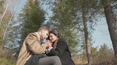 Genç bir erkek ve kadın, doğada huzurlu bir anın tadını çıkarırlar, el ele tutuşurlar ve birbirlerinin gözlerine bakarlar. Sakin orman düzeni, romantik atmosferi ve duygusal bağlantıyı güçlendirir.