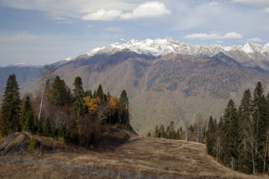Krasnaya Polyana, Sochi, Kuzey Kafkasya dağları, sonbahar ağaçlarının arka planında karla kaplı tepeler,