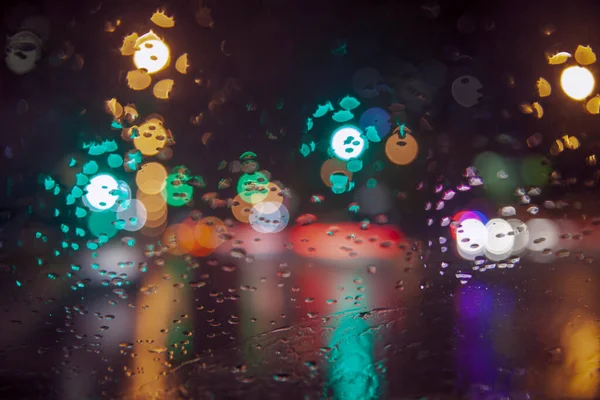 Rainy weather, night city, raindrops through the glass, abstract background from the light of cars and traffic lights, defocus, rain drops on car glass in rainy night, toned