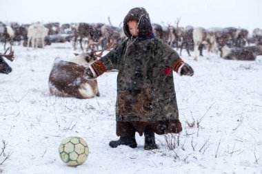 Yamal Yarımadası. Genç bir ren geyiği çobanı. Ren geyiği otlağındaki mutlu çocuk kışın bir topla oynuyor..