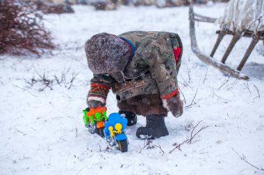 Yamal Yarımadası. Genç bir ren geyiği çobanı. Ren geyiği otlağındaki mutlu çocuk kışın oyuncak motorsikletle oynuyor..