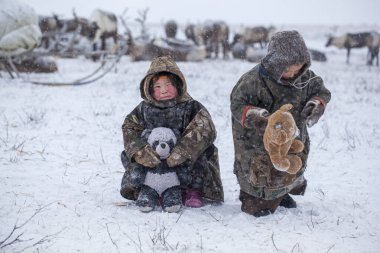 Yamal Yarımadası, en kuzeyde. Soğuk bir kış gününde ren geyiği otlağı üzerinde mutlu bir oğlan ve kız, kutup dairesi, çocuklar ve hayvanlar.