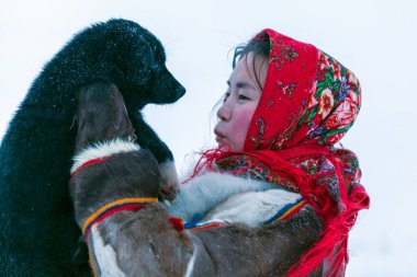 Tundra 'nın kuzey sakinlerinin ulusal kış kıyafetleri içinde genç bir kız bir köpekle oynuyor.