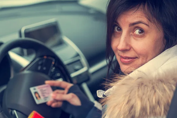 Getting a driver's license, female hands show US driving license, amid the steering wheel of a car, toned