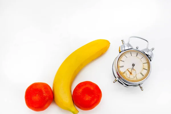 Creative concept of male potency problems. A curved banana with tangerines hangs over an old alarm clock showing the time at half past five. Sexual dysfunction in men, problems with health. Erectile dysfunction impotence