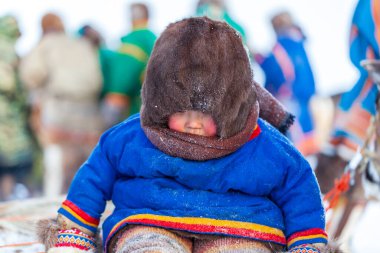 Nadym, Rusya - 23 Şubat 2020: Uzak Kuzey, Yamal Yarımadası, Ren Geyiği Çobanı Günü, Nenets 'in ulusal kıyafetleri içinde yerel halk, kızak içindeki küçük çocuk