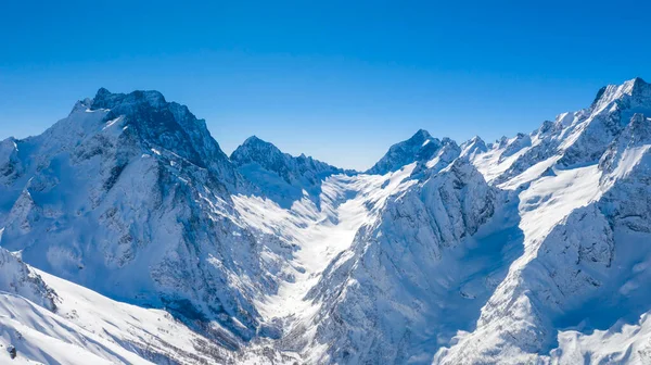 Kafkasya Dağları, Belalakaya, Sofrudzhu ve Sulakhat dağları ile kayak yamacının panoramik manzarası kış günü ufukta. Dombai kayak merkezi, Batı Kafkasya, Karachai-Cthe, Rusya, hava fotoğrafı..