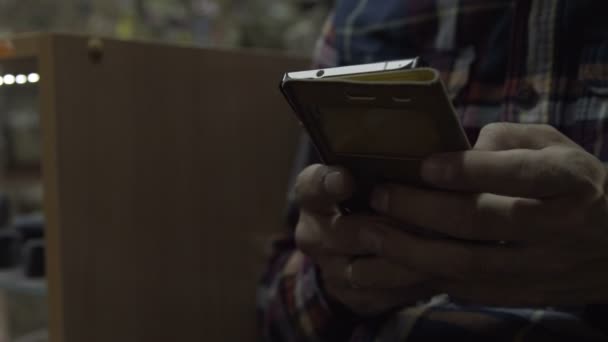 L'homme entre les mains du téléphone. Le gars assis sur une chaise tenant un smartphone — Video