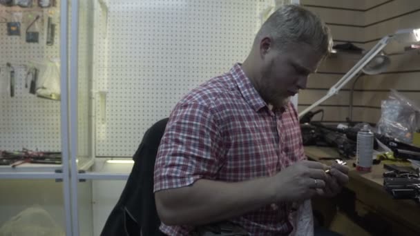 Man reparera vapen. Killen med skägget rensar och reparerar armekie gevär och pistoler vid sitt skrivbord i studio — Stockvideo