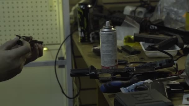 Человек чинит оружие. Парень с бородой чистит и ремонтирует армейские винтовки и пистолеты за своим столом в мастерской — стоковое видео