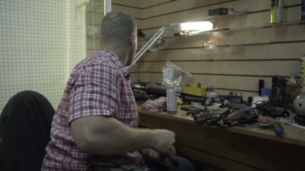 Hombre reparando armas. El tipo con la barba limpia y repara rifles y pistolas armekie en su escritorio en el estudio — Vídeos de Stock