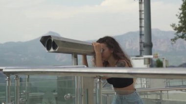 Kadın gözlem güvertesindeki tepelere dürbünle bakıyor.