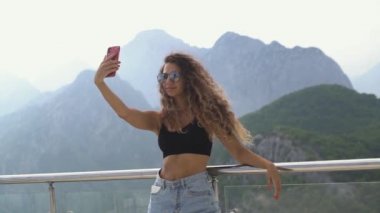 Çekici bayan, dağlara karşı korkulukların yanında selfie çekiyor.