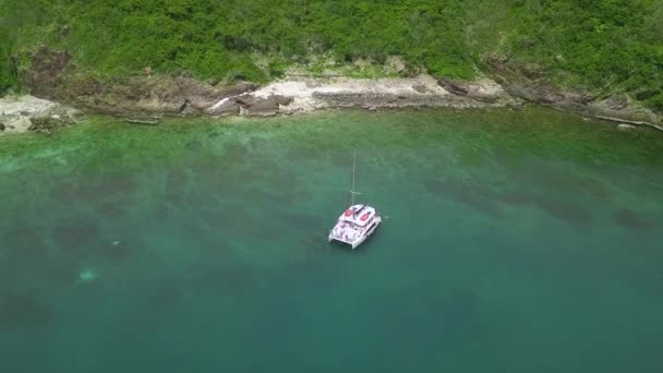 Jacht z opuszczonymi żaglami dryfuje na spokojnym oceanie w pobliżu wybrzeża — Wideo stockowe