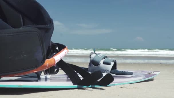 Tabla de kitesurf de color azul se encuentra en la playa de arena amarilla — Vídeos de Stock