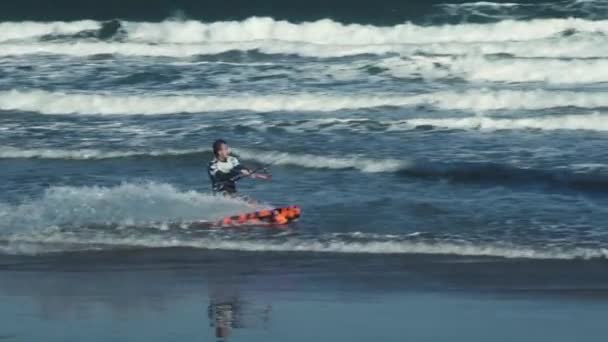 Kite surfer σε μαύρο πορτοκαλί πίνακα πιάνει τα κύματα κάνοντας κόλπα — Αρχείο Βίντεο