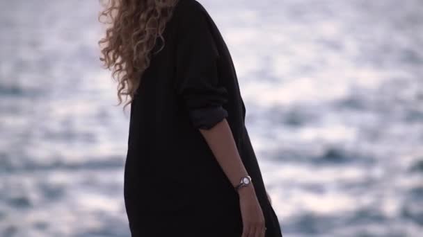 Elegancka młoda kobieta wędruje wzdłuż plaży w pobliżu rozmytego morza — Wideo stockowe