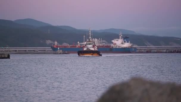 Motorboot vaart op zeehaven tegen schip en heuvelachtige kust — Stockvideo