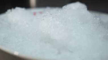 Masanın üzerinde duran buz parçalarını boş tabağa koyar