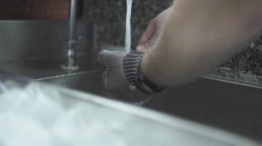 Metal eldivenli bir adam lavabonun üzerinde bıçakla istiridye açar.