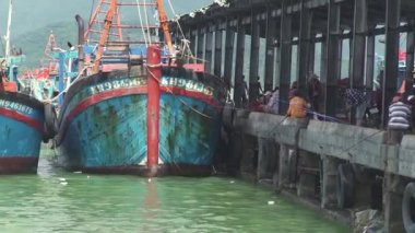 Asyalılar, demirli teknelerin yakınındaki eski ahşap iskelede balık tutuyor.